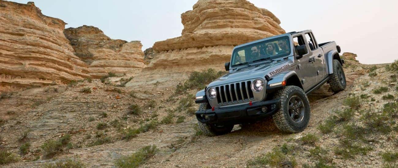 A silver 2020 Jeep Gladiator is off-roading with passengers on a desert trail.