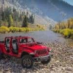 A new red 2020 Jeep Gladiator crosses a large river at the foot of a mountain