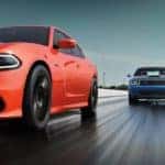 An orange 2018 Dodge Charger is racing a blue Challenger on a wet track. Oranger County Dodge Dealers are a great place to check one out.