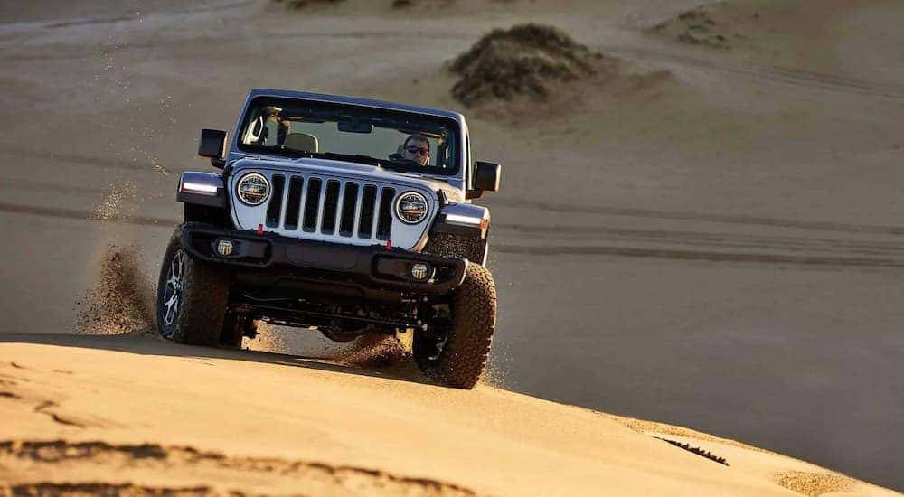 A silver 2019 Jeep Wrangler Rubicon is driving on the sand near Costa Mesa, CA.