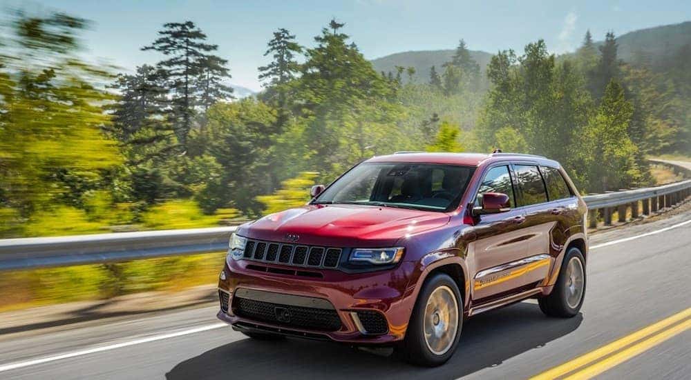 A red 2019 Jeep Grand Cherokee Trackhawk is driving down a highway with mountains.
