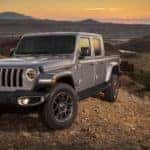 A grey 2020 Jeep Gladiator is parked high up with mountains in the distance and a setting sun.