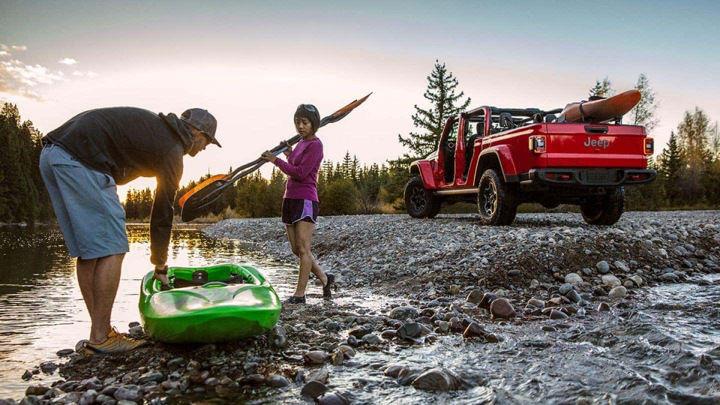 A red 2020 Jeep Gladiator with two Kayakers next to a river