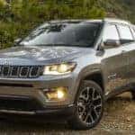 A grey 2020 Jeep Compass is parked on a dirt trail that's overlooking trees.
