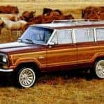 A red and wood-sided 1991 Jeep Grand Wagoneer is parked in a pasture with horses.