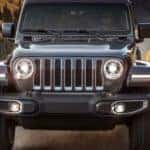 A 2020 grey Jeep Wrangler is driving on a windy road with mountains in the distance facing forward.
