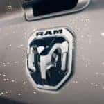 A close up of the Ram logo on a silver tailgate is shown with lights shining on it.