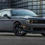 A grey 2018 Dodge Challenger, which is a popular performance vehicle that you could find at a used car dealer, is parked in front a glass building near Costa Mesa, CA.
