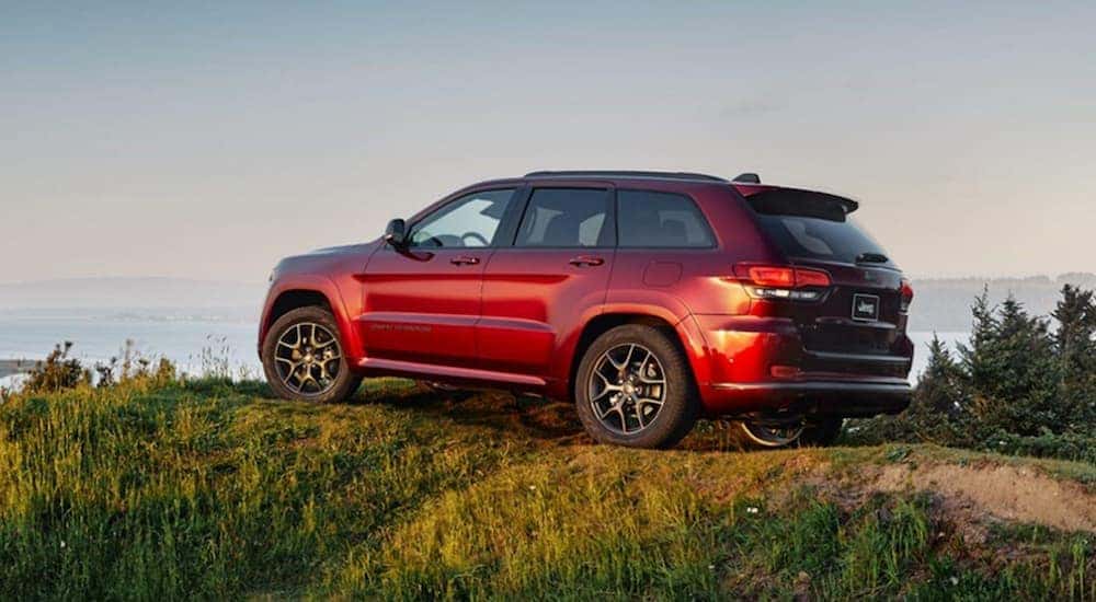 A red 2020 Jeep Grand Cherokee for sale is parked on a hill that's overlooking a beach at dusk.