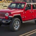 A red topless 2020 Jeep Wrangler is driving on a rock lined road outside of Costa Mesa, CA.