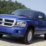 A blue 2011 Dodge Dakota, which is a model you may find used at a Ram dealership in Costa Mesa, CA, is driving on a treelined highway near Costa Mesa, CA.