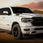 A white 2020 Ram 1500, Night Edition, is driving on a road near Costa Mesa, CA, with the sun sets behind it.