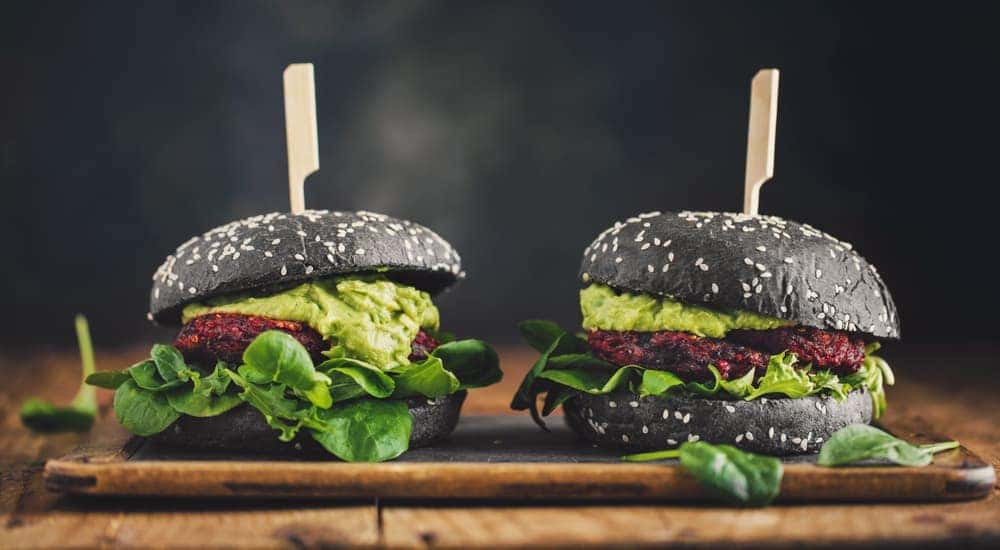 Two black vegan burgers are on a wooden platter.