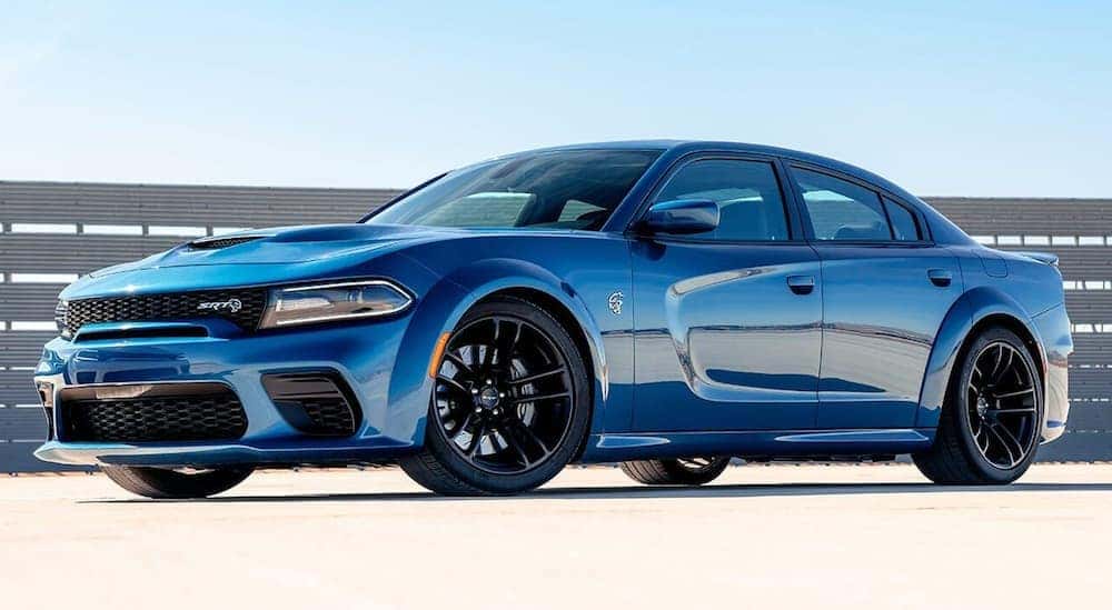 A blue 2019 Dodge Charger is parked in an empty parking lot with a metal fence behind it.