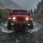 A red 2020 Jeep Wrangler is driving through a stream in the rain.