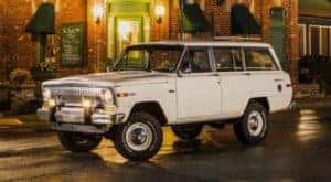A classic white Jeep Wagoneer is driving on a city street outside Costa Mesa, CA.