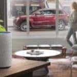 A woman is looking out the window at a red 2020 Jeep Grand Cherokee while an Alexa is in the foreground.