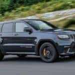 A black 2018 Jeep Grand Cherokee is driving on a tree-lined highway after leaving a used car dealer near Costa Mesa, CA.