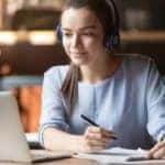 A girl with headphones on is taking notes while doing an online class in Costa Mesa, CA.