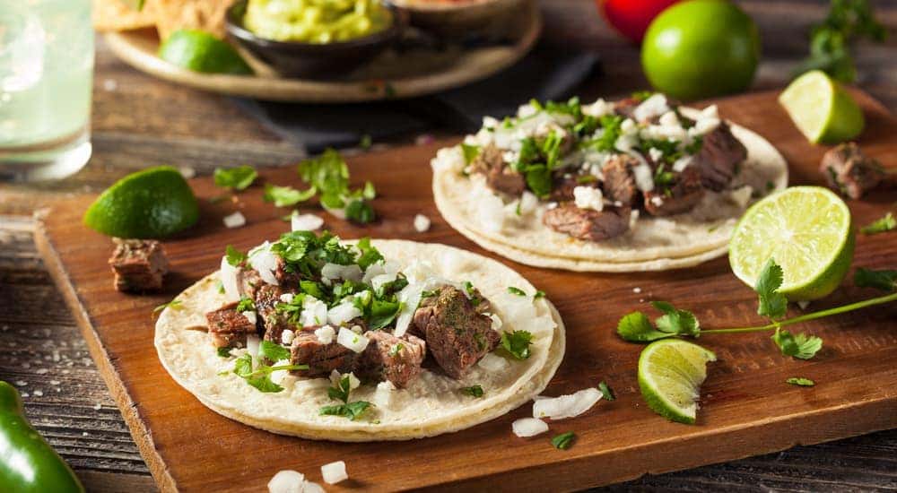 Two tacos are shown with limes on a wood platter.