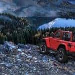 A red 2020 Jeep Wrangler is parked above a mountain lake while off-roading after leaving a Jeep dealership in Costa Mesa, CA.