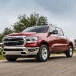 A red 2020 Ram 1500, which is popular among Ram trucks, is driving past a white fence and field.
