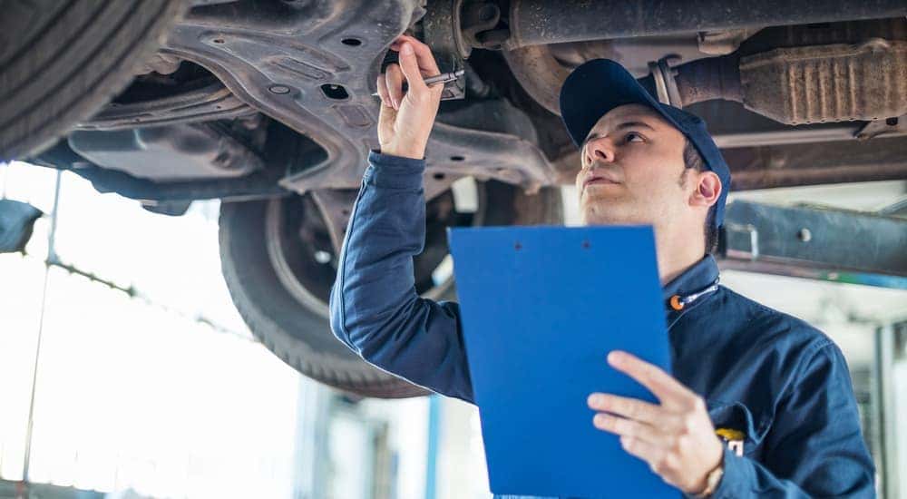 A mechanic in Costa Mesa, CA, is working under a car with a blue clipboard in his hand.
