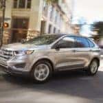 A silver 2018 Ford Edge is driving through a city intersection.