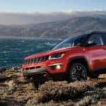 A red 2020 Jeep Compass Trailhawk is parked on rocks at a beach near Costa Mesa, CA.