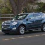 A dark blue 2016 Chevy Equinox is driving on a fence-lined road.