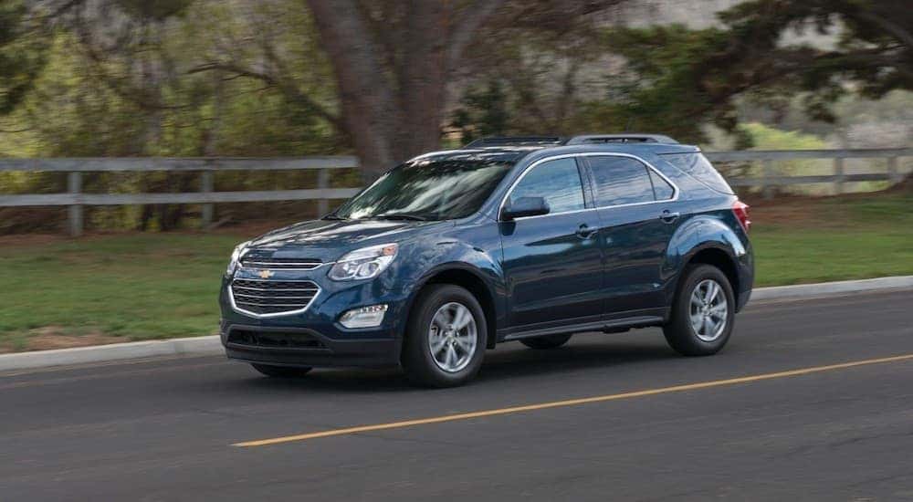 A dark blue 2016 Chevy Equinox is driving on a fence-lined road.