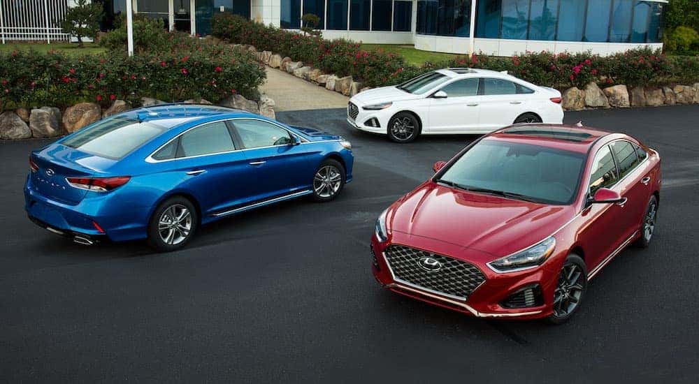 A red, a blue, and a white 2018 Hyundai Sonata are parked in front of a white building near Costa Mesa, CA.