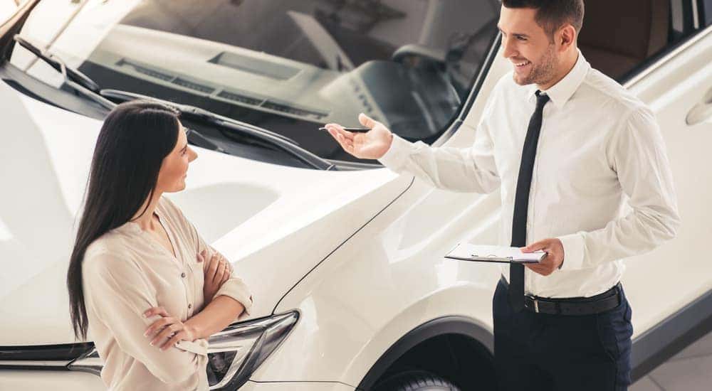 A woman is talking to a salesman in front of a white car at a used car dealership near me.