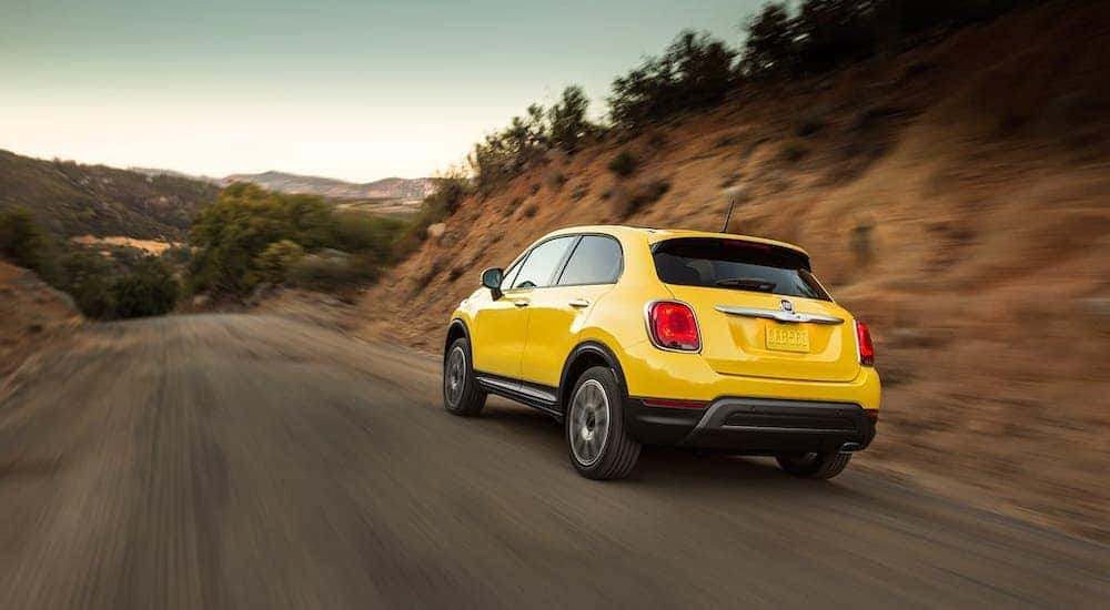 A yellow 2018 Fiat 500X is driving towards a mountainous road outside Costa Mesa, CA.