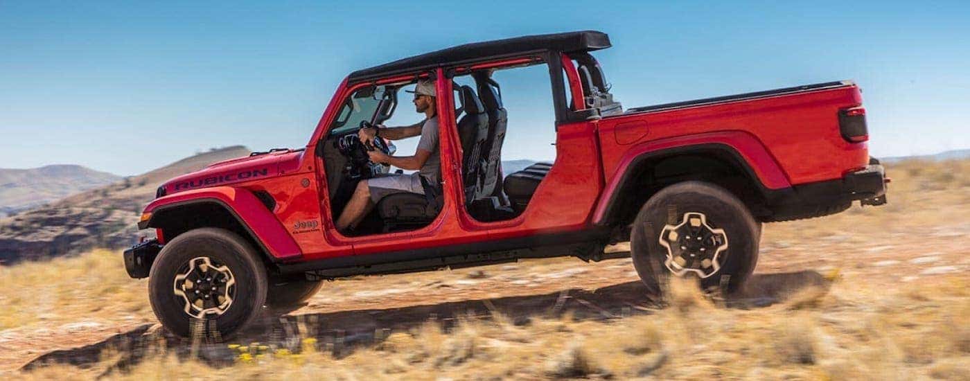 A red Gladiator with no doors is shown from the side driving in a field after winning the 2020 Jeep Gladiator vs 2020 Chevy Colorado comparison.
