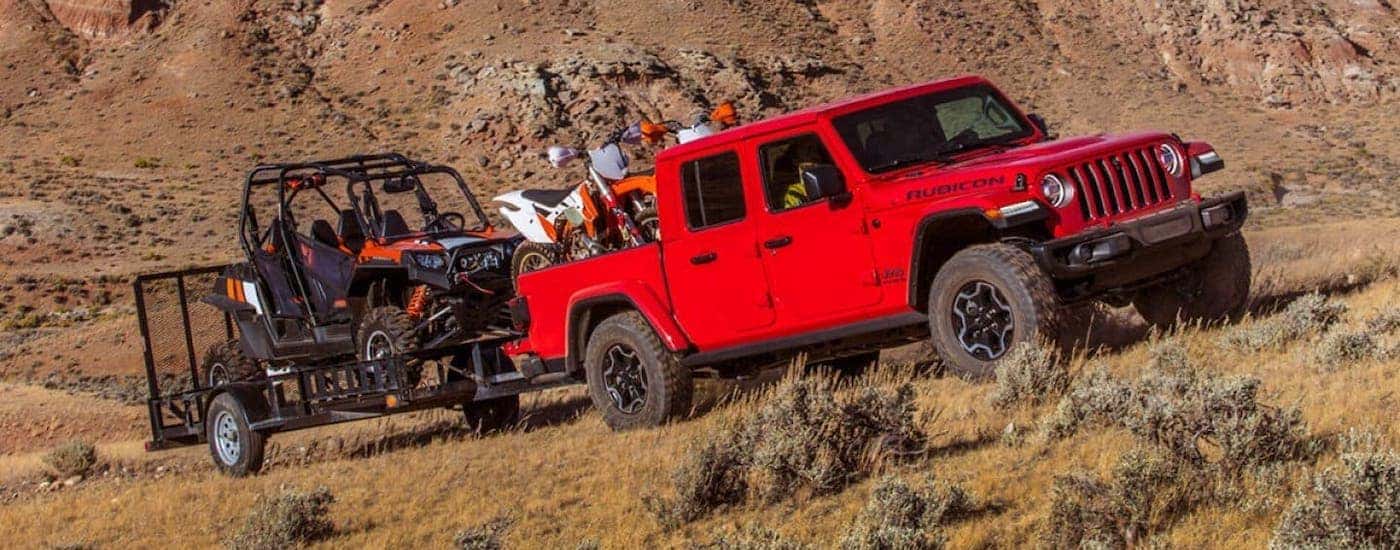 A red 2020 Jeep Gladiator is towing a side-by-side and dirt bikes in a desert outside Costa Mesa.