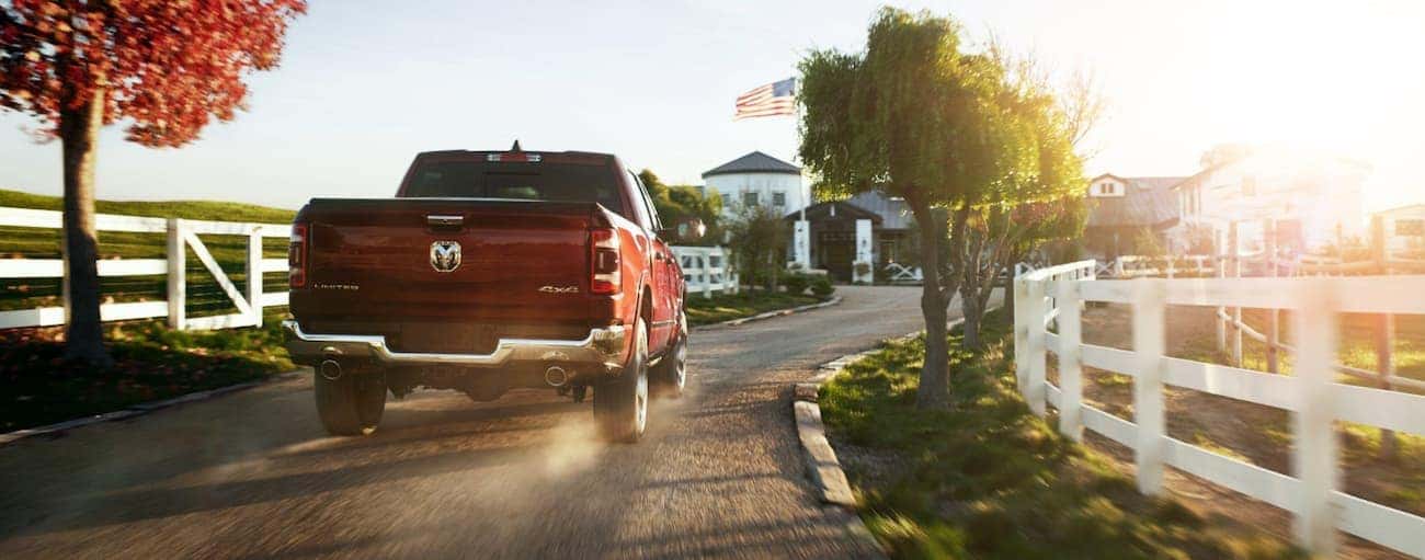 A red 2020 Ram 1500 is driving down a dirt driveway toward a farm after winning the 2020 Ram 1500 vs 2020 GMC Sierra 1500 comparison.