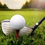 A closeup is showing a ball on a tee and a driver about to hit it.
