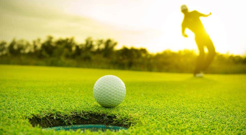 A golf ball is just outside a hole while a silhouette of a man is leaning in the background.