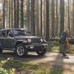 Two hikers are walking away from a gray 2020 Jeep Wrangler Unlimited that is parked in the woods.