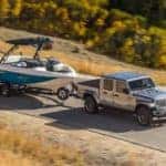 A silver 2020 Jeep Gladiator is towing a boat on a highway, shown from a high angle.