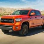 An orange 2015 Toyota Tundra is driving past desert mountains.