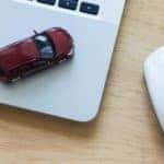A red toy car is on a laptop next to a mouse.