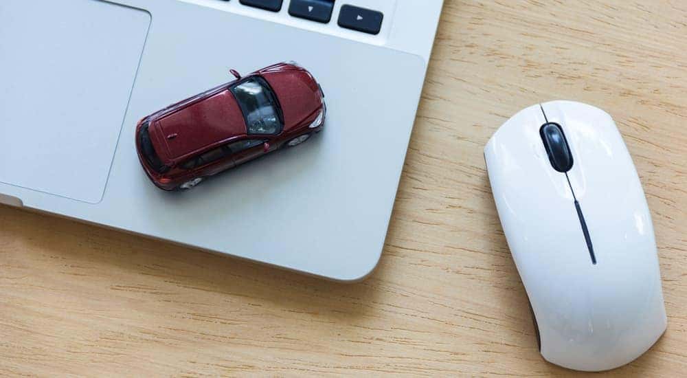 A red toy car is on a laptop next to a mouse.