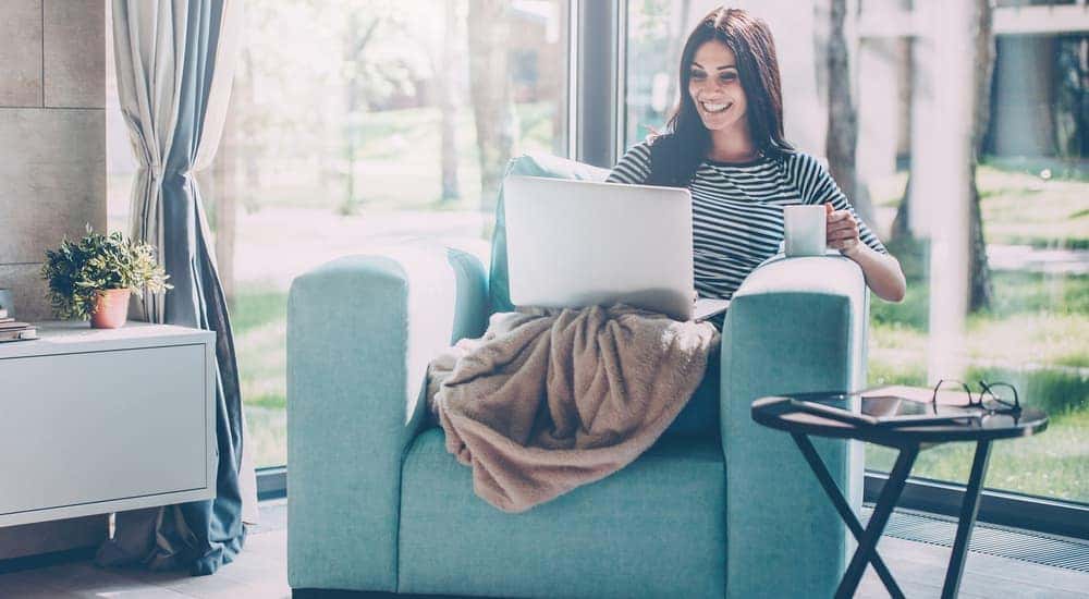 A woman is smiling using her laptop while sitting in a blue chair.