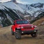 A red 2018 Jeep Wrangler Rubicon with no roof is driving on a dirt trail.
