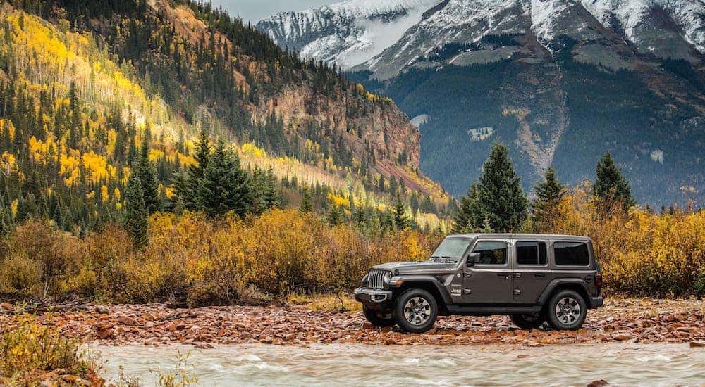 Arguable the best used SUV for sale, a gray 2018 Jeep Wrangler Unlimited is parked next to a river in front of mountains.