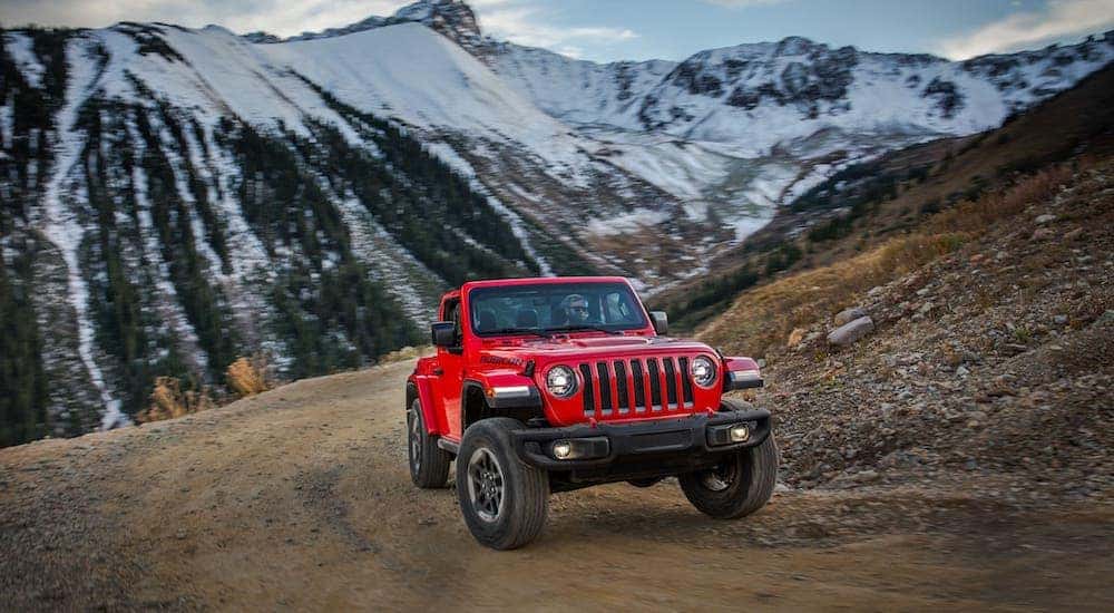 A red 2018 Jeep Wrangler Rubicon with no roof is driving on a dirt trail.