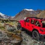 A red 2020 Jeep Wrangler Unlimited with no roof is climbing over rocks against a vibrant blue sky.