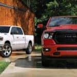 A red and a white 2020 Ram 1500 are parked in front of a barn.
